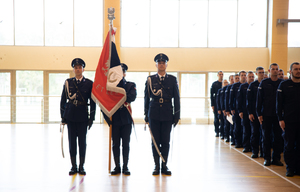 Po lewej stronie policjanci Centrum Szkolenia Policji w Legionowie stoją w poczcie sztandarowym  sztandarem. Po prawej stronie stoją słuchacze.