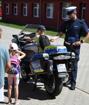 Chłopiec siedzący na motocyklu policyjnym. Obok stoi policjant z Zakładu Ruchu Drogowego i dziewczynka.